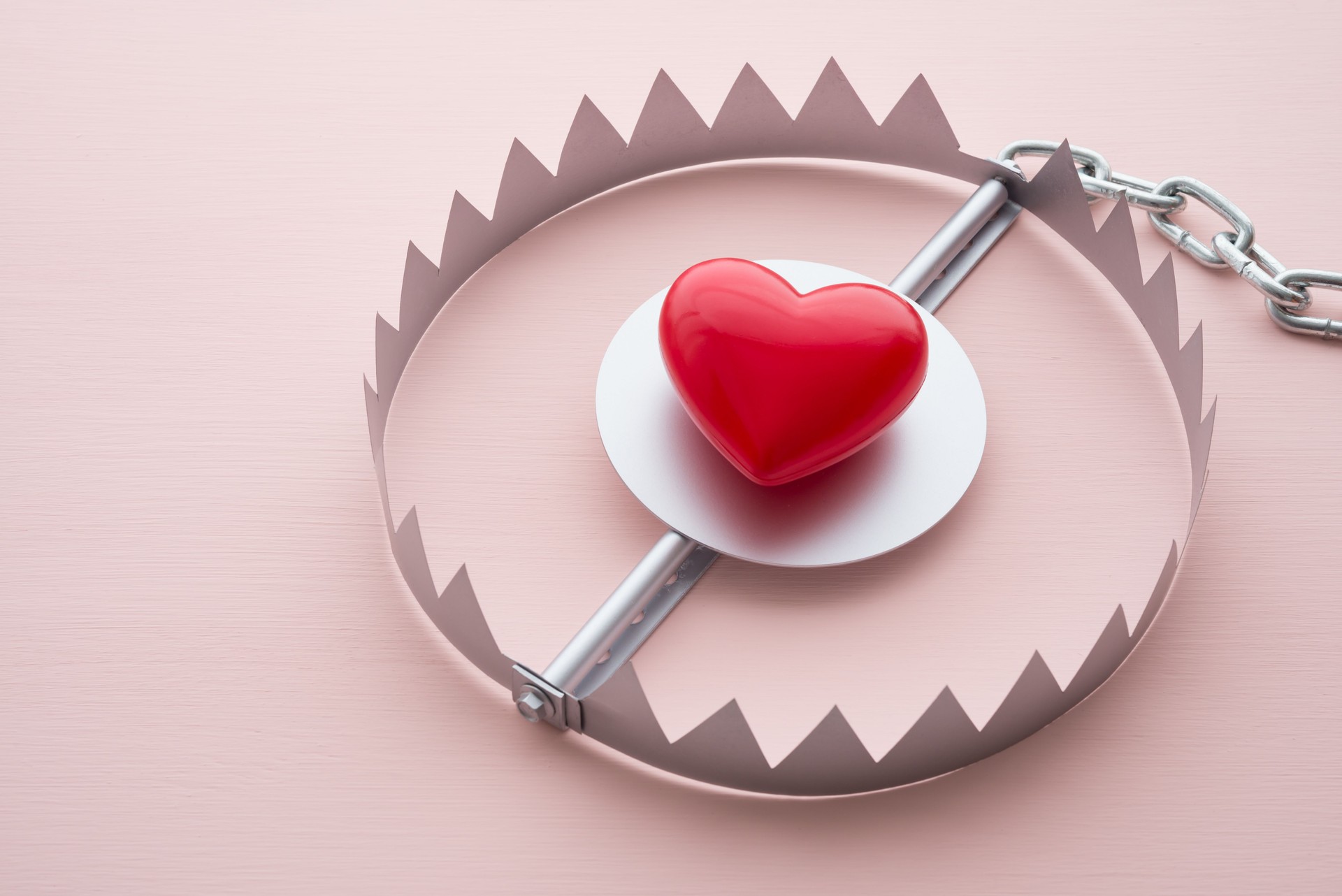 Red heart in a trap on pink background.